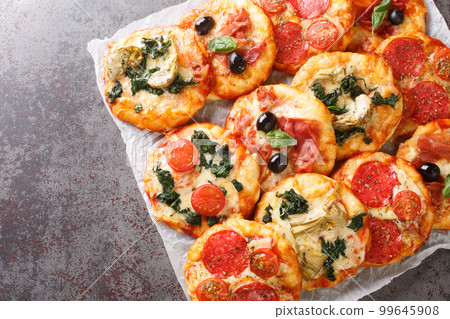 Italian Pizzette Mini Pizza Bites With Assorted Toppings close-up on parchment. Horizontal top view 99645908