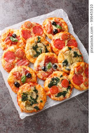 Homemade Mini Pizzas Pizzette with meaty and vegetarian toppings close-up on parchment. Vertical top view Homemade Mini Pizzas Pizzette with meaty and vegetarian toppings close-up on parchment. Vertical top view 99645910