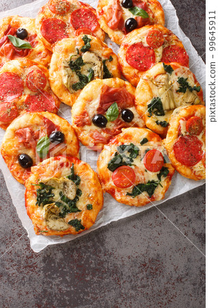 Pizzette small pizzas with various toppings close-up on parchment. Vertical top view Pizzette small pizzas with various toppings close-up on parchment. Vertical top view 99645911