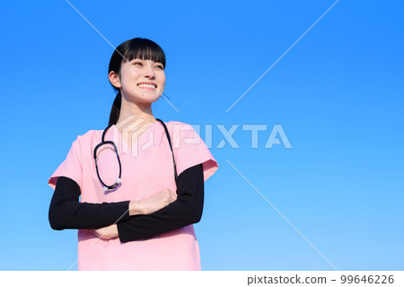 A female nurse wearing a scrub standing with her arms crossed against the blue sky, a medical worker, a doctor, an outpatient examination, A female nurse wearing a scrub standing with her arms crossed against the blue sky, a medical worker, a doctor, an outpatient examination, 99646226