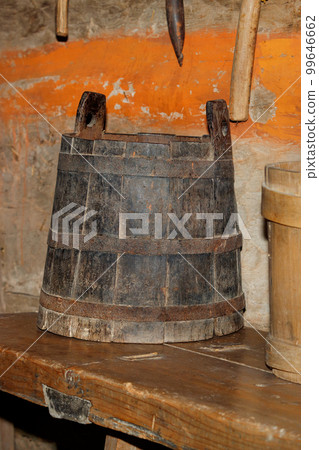 An old ancient wooden bucket with forged metal hoops on a wooden bench. An old ancient wooden bucket with forged metal hoops on a wooden bench. 99646662