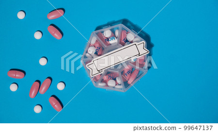 Closeup of medical pill box with doses of tablets for daily take medicine with white pink drugs and capsules with paper note Copy space for your text template mock up. Daily vitamins at home. Health Closeup of medical pill box with doses of tablets for daily take medicine with white pink drugs and capsules with paper note Copy space for your text template mock up. Daily vitamins at home. Health 99647137