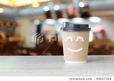 Paper cup of coffee on the table with a smile symbol on blur cafe background. Paper cup of coffee on the table with a smile symbol on blur cafe background. 99647264