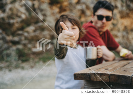 School boy kid child shows thumb up while having a family picnic in the mountains with his father dad 99648898