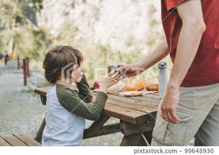Close-up view of father and his school boy son on a family picnic in the mountains. Child kid and his dad taking a rest and enjoying a picnic while hiking in the mountains 99648930