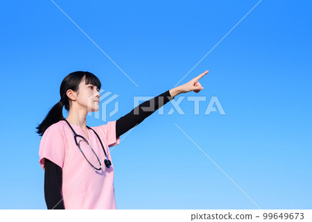 A female nurse wearing a scrub standing against the blue sky, a medical worker, a doctor, an outpatient, an examination, pointing 99649673