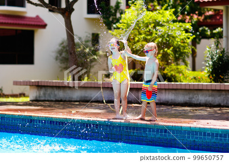Kids play with water hose at swimming pool. 99650757