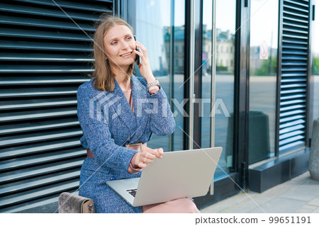 Business woman working on street. Young woman is sitting on bench with laptop 99651191