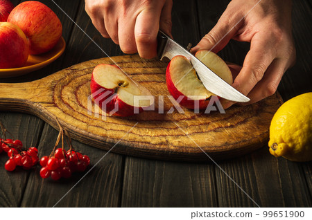 Cook cuts apples on a cutting board to make compote or fruit juice. Apple diet for a set of vitamins. Work environment on the kitchen table 99651900