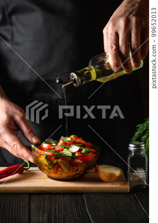 The chef pours olive oil into a bowl of salad. Cooking tasty and healthy food with set of vitamins 99652013