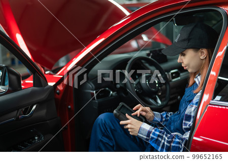 Caucasian female auto mechanic uses a special computer to diagnose faults. Caucasian female auto mechanic uses a special computer to diagnose faults. 99652165