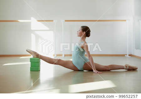 Professional ballet dancer, teen girl training at ballet school indoors on daytime. Doing stretching with yoga blocks. Concept of classical ballet, art, choreography 99652257