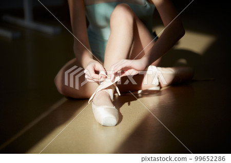 Cropped image of female ballerina legs, girl putting on pointe shoes. Model in ballet studio, school on daytime with sunlight. Concept of classical ballet, art, choreography Cropped image of female ballerina legs, girl putting on pointe shoes. Model in ballet studio, school on daytime with sunlight. Concept of classical ballet, art, choreography 99652286