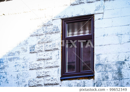 Brown plastic window in white wide brick wall with bright sun beam on the corner of the building Brown plastic window in white wide brick wall with bright sun beam on the corner of the building 99652349