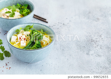 Vegan laksa with rice noodles, broccoli and tofu in blue bowls, gray background. 99652655