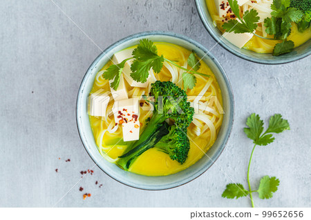 Vegan laksa with rice noodles, broccoli and tofu in blue bowls, gray background. Vegan laksa with rice noodles, broccoli and tofu in blue bowls, gray background. 99652656