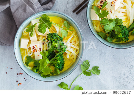 Vegan laksa with rice noodles, broccoli and tofu in blue bowls, gray background. Vegan laksa with rice noodles, broccoli and tofu in blue bowls, gray background. 99652657