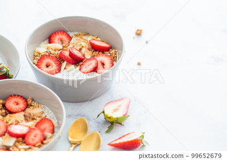 Chia pudding with homemade coconut granola, peanut butter and strawberries in a gray bowl, marble background. Healthy diet, detox, summer recipe. 99652679