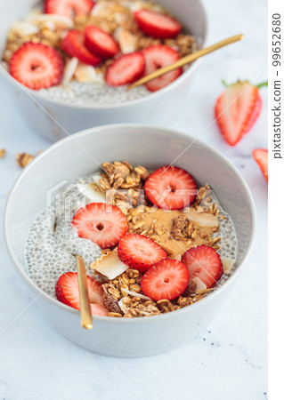 Chia pudding with homemade coconut granola, peanut butter and strawberries in a gray bowl, marble background. Healthy diet, detox, summer recipe. Chia pudding with homemade coconut granola, peanut butter and strawberries in a gray bowl, marble background. Healthy diet, detox, summer recipe. 99652680