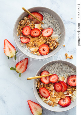 Chia pudding with homemade coconut granola, peanut butter and strawberries in a gray bowl, marble background. Healthy diet, detox, summer recipe. Chia pudding with homemade coconut granola, peanut butter and strawberries in a gray bowl, marble background. Healthy diet, detox, summer recipe. 99652681