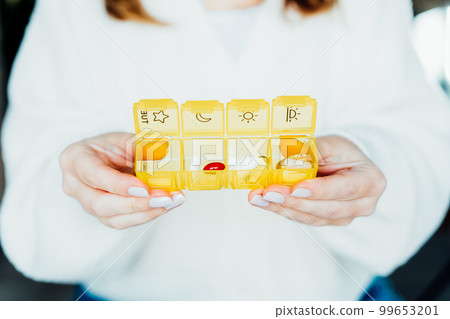 Close up Female hands holding opened daily pills organizer. Taking daily medicine antioxidant diet vitamin supplements for beauty skin hair health care medicament biohacking concept. Selective focus 99653201