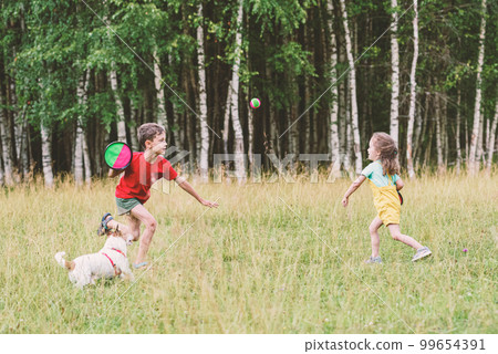 Kids and family pet dog playing with toss and catch ball set outdoors. Activity game during picnic in nature park Kids and family pet dog playing with toss and catch ball set outdoors. Activity game during picnic in nature park 99654391