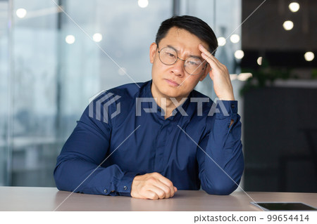 Portrait of overworked and tired office worker at workplace, asian man in glasses and shirt looking upset at camera, businessman not satisfied with work and own results achievement in depression. Portrait of overworked and tired office worker at workplace, asian man in glasses and shirt looking upset at camera, businessman not satisfied with work and own results achievement in depression. 99654414