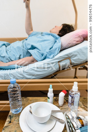 cup, medicines and patient holding handle on bed 99654476