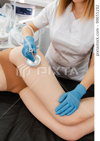 Cosmetologist reducing cellulite on hips of female patient Cosmetologist reducing cellulite on hips of female patient 99655282