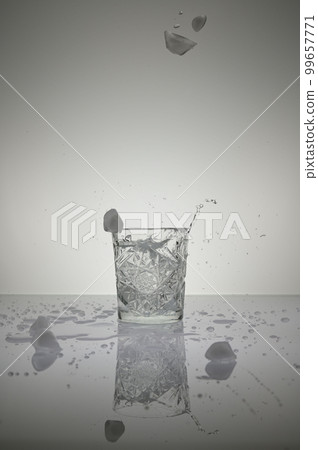 Vertical shot of ice cubes falling into a crystal water glass,isolated on a wet shiny white surface Vertical shot of ice cubes falling into a crystal water glass,isolated on a wet shiny white surface 99657771