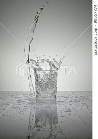 Vertical shot of crystal water glass with water splash and droplets around, on a white shiny table 99657774