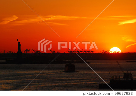 Silhouette of Statue of Liberty and Liberty Island in New York against an orange sunset sky 99657928