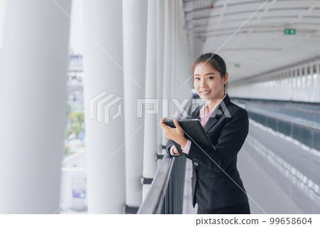young Asian businesswoman in black suit using digital tablet and standing on walkway station with copy space. young Asian businesswoman in black suit using digital tablet and standing on walkway station with copy space. 99658604