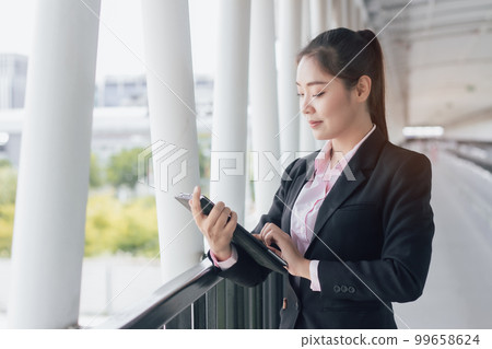young Asian businesswoman in black suit using digital tablet and standing on walkway station with copy space. 99658624