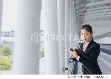 young Asian businesswoman in black suit using digital tablet and standing on walkway station with copy space. 99658627