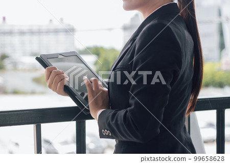 young Asian businesswoman in black suit using digital tablet and standing on walkway station with copy space. 99658628