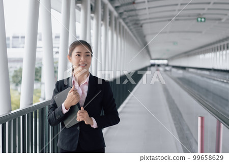 young Asian businesswoman in black suit using digital tablet and standing on walkway station with copy space. 99658629