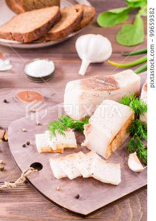 Sliced salted lard with garlic and dill on a cutting board on a wooden table 99659382