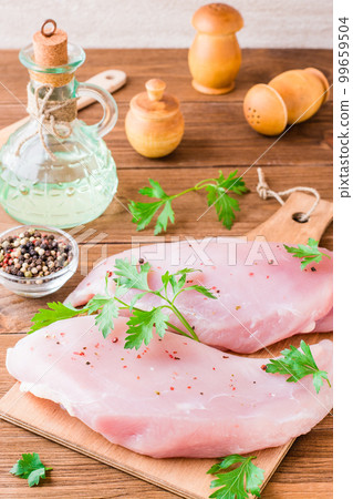 Raw turkey fillet in spices and herbs on a cutting board on a wooden table Raw turkey fillet in spices and herbs on a cutting board on a wooden table 99659504