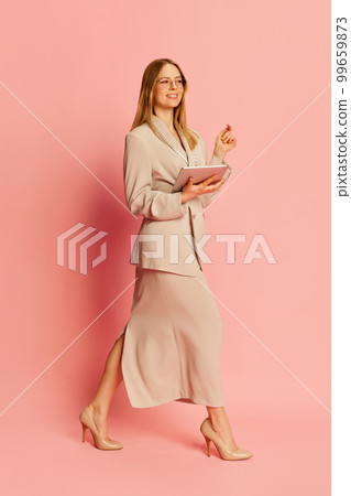 Happy young pretty blonde girl, student wearing modern office style clothes using tablet over pink background. Concept of youth, student college life, business and education. 99659873
