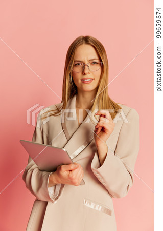 Happy young pretty blonde girl, student wearing modern office style clothes using tablet over pink background. Concept of youth, student college life, business and education. 99659874
