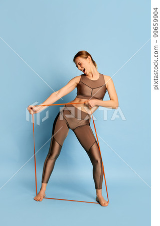 Happy young beautiful girl in sports fitness clothes doing exercises, training over blue background. Sport, fitness, happy positive emotions and active lifestyle concept. 99659904