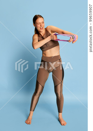 Happy young beautiful girl in sports fitness clothes doing exercises, training over blue background. Sport, fitness, happy positive emotions and active lifestyle concept. 99659907