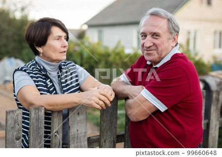 Two gardeners friendly talking outdoors next to wooden fence of country estate on day Two gardeners friendly talking outdoors next to wooden fence of country estate on day 99660648