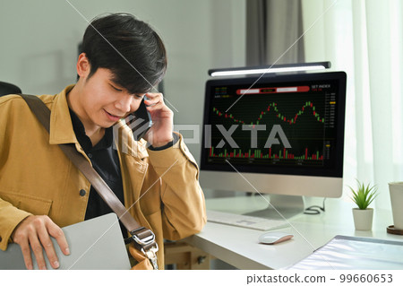 Man trader sitting front of computer monitor with digital exchange stock market charts graphs and talking on mobile phone 99660653