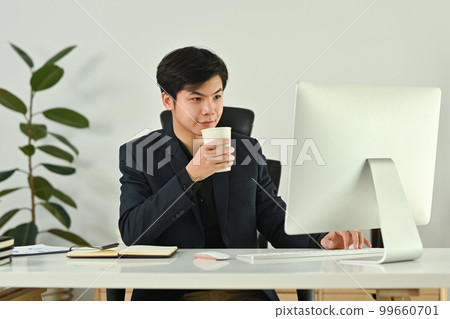 Successful asian man business entrepreneur drinking coffee and reading email on computer screen Successful asian man business entrepreneur drinking coffee and reading email on computer screen 99660701
