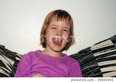 Girl sits on the sofa and eats dried apples. The child is laughing, happy and healthy Girl sits on the sofa and eats dried apples. The child is laughing, happy and healthy 99660968