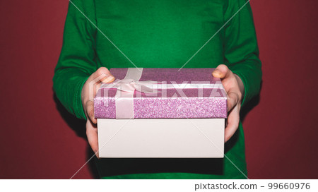 Close-up of children's hands holding a box with a gift on a red background. Holiday concept. 99660976