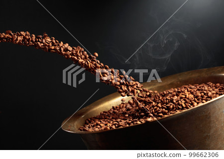 Medium-roasted coffee beans are poured into an old brass roasting pan. 99662306