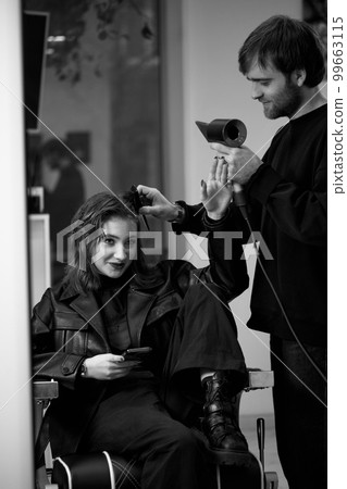 man hairdresser dries female hair with hairdryer after washing 99663115